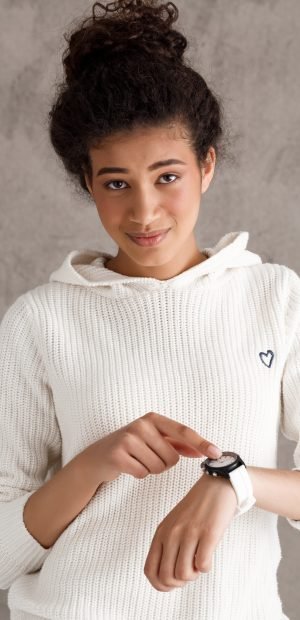 Young beautiful african girl pointing finger at wristwatch over beige background. Copy space.