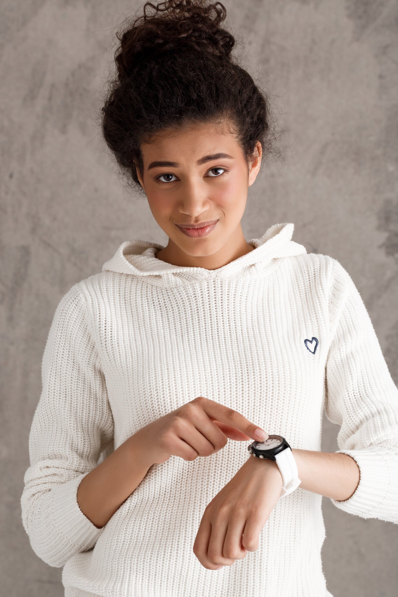 Young beautiful african girl pointing finger at wristwatch over beige background. Copy space.